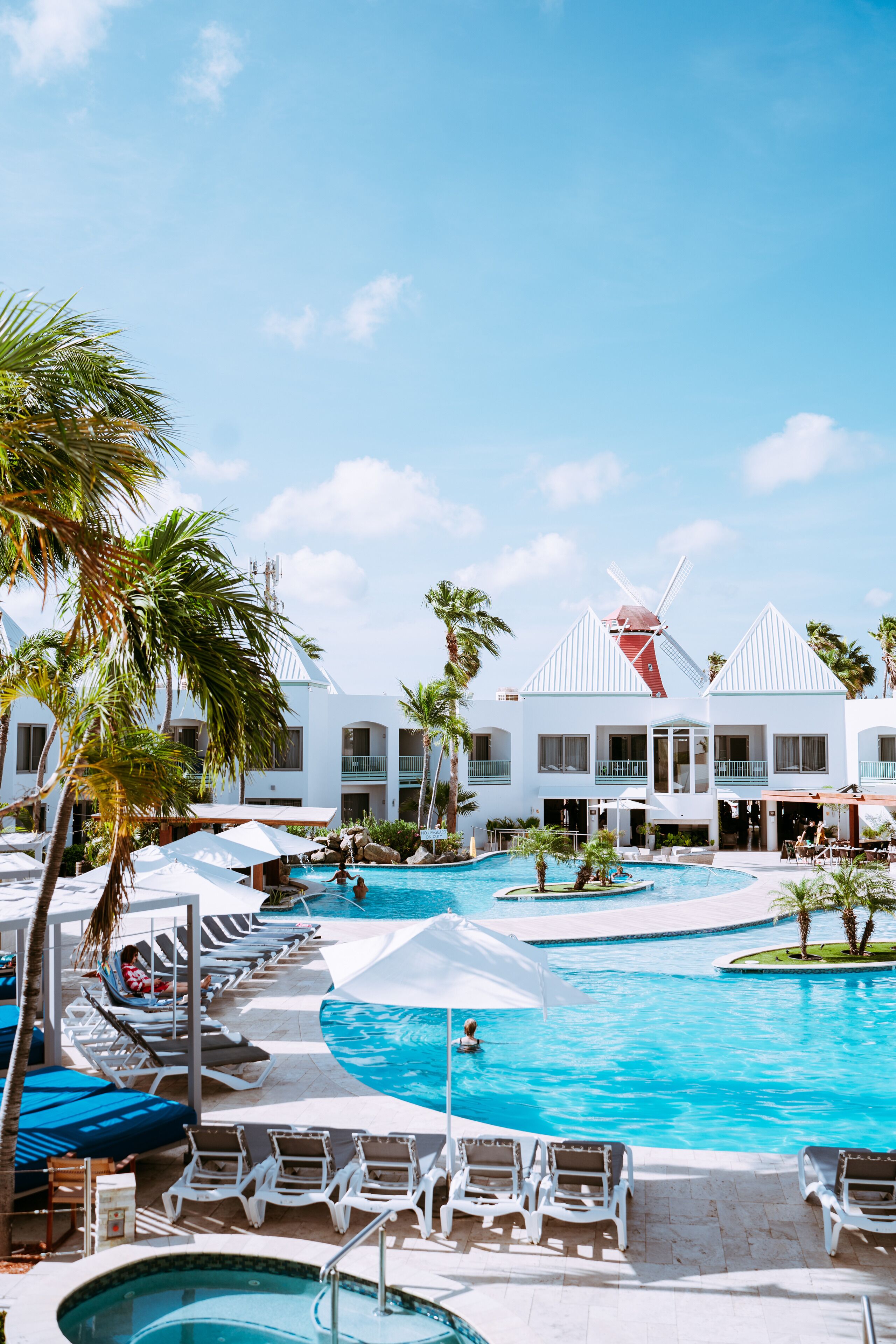 Un resort con una amplia piscina, palmeras y molinos.