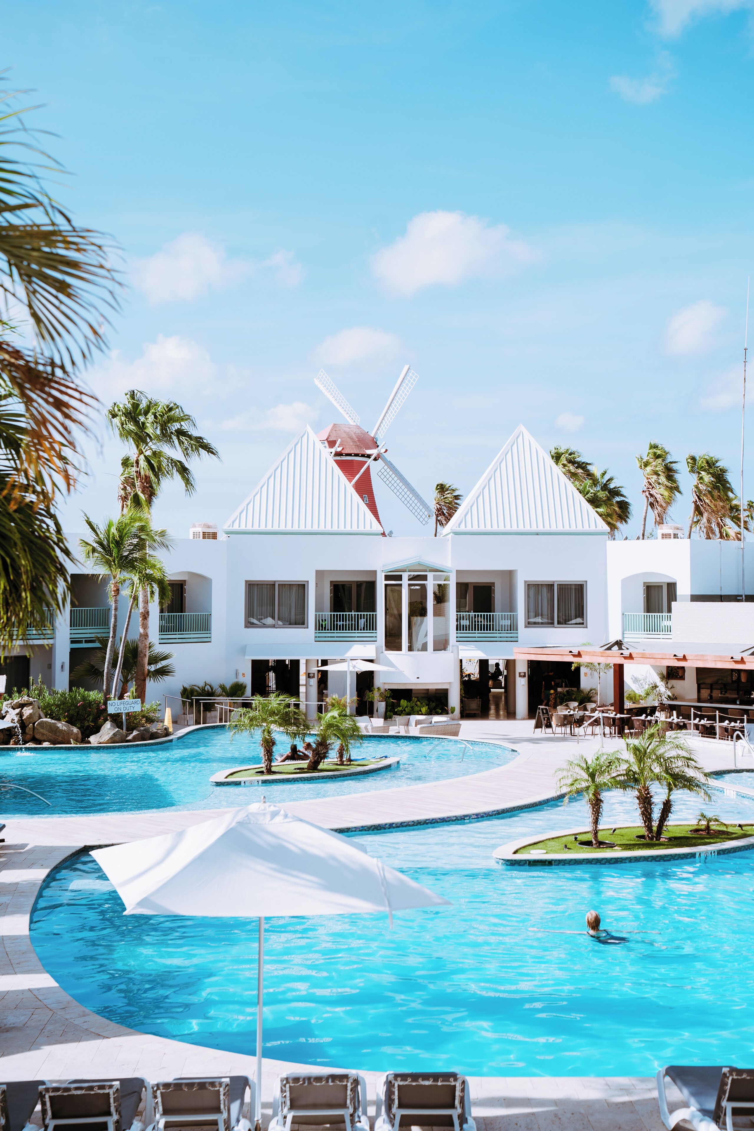 Un resort con un amplio área de piscina, palmeras y una estructura de molino.