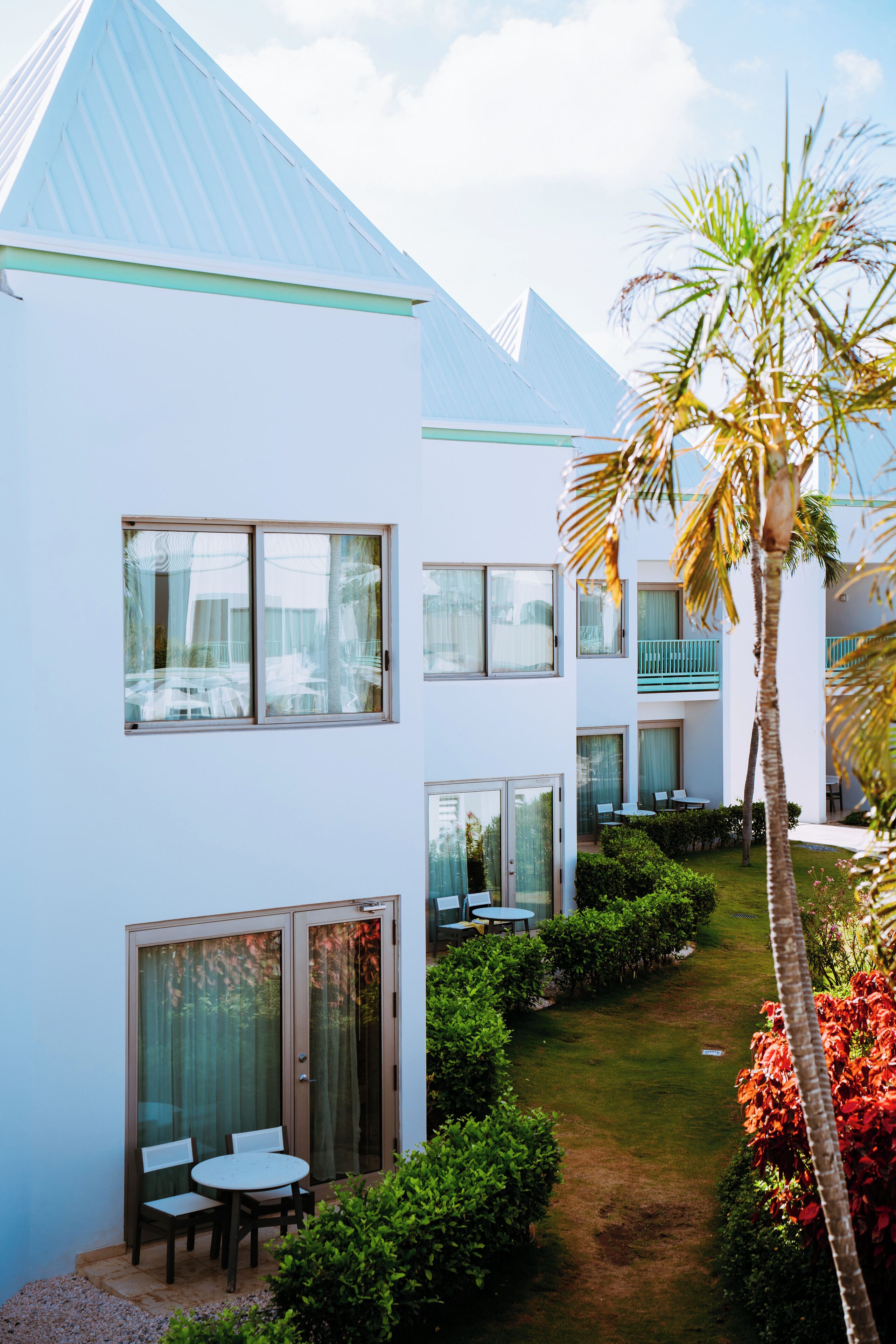 A modern hotel with a courtyard, including a seating area with tables and chairs, and a palm tree.