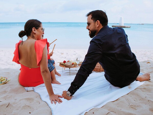 A couple sitting on a beach towel with a picnic setup, including a basket and a glass of wine.