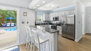 A modern kitchen with white cabinets, stainless steel appliances, and a bar area with white stools. - Private Pool, 6 passenger Golf Cart, and 4 bikes! EV charger on site! (Destin)
