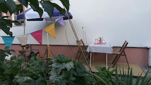 Un patio con una mesa y sillas, una pequeña mesa con una planta en maceta y banderas de colores.