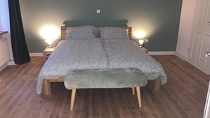 Un dormitorio con una cama, lámparas de noche, un banco y suelo de madera.