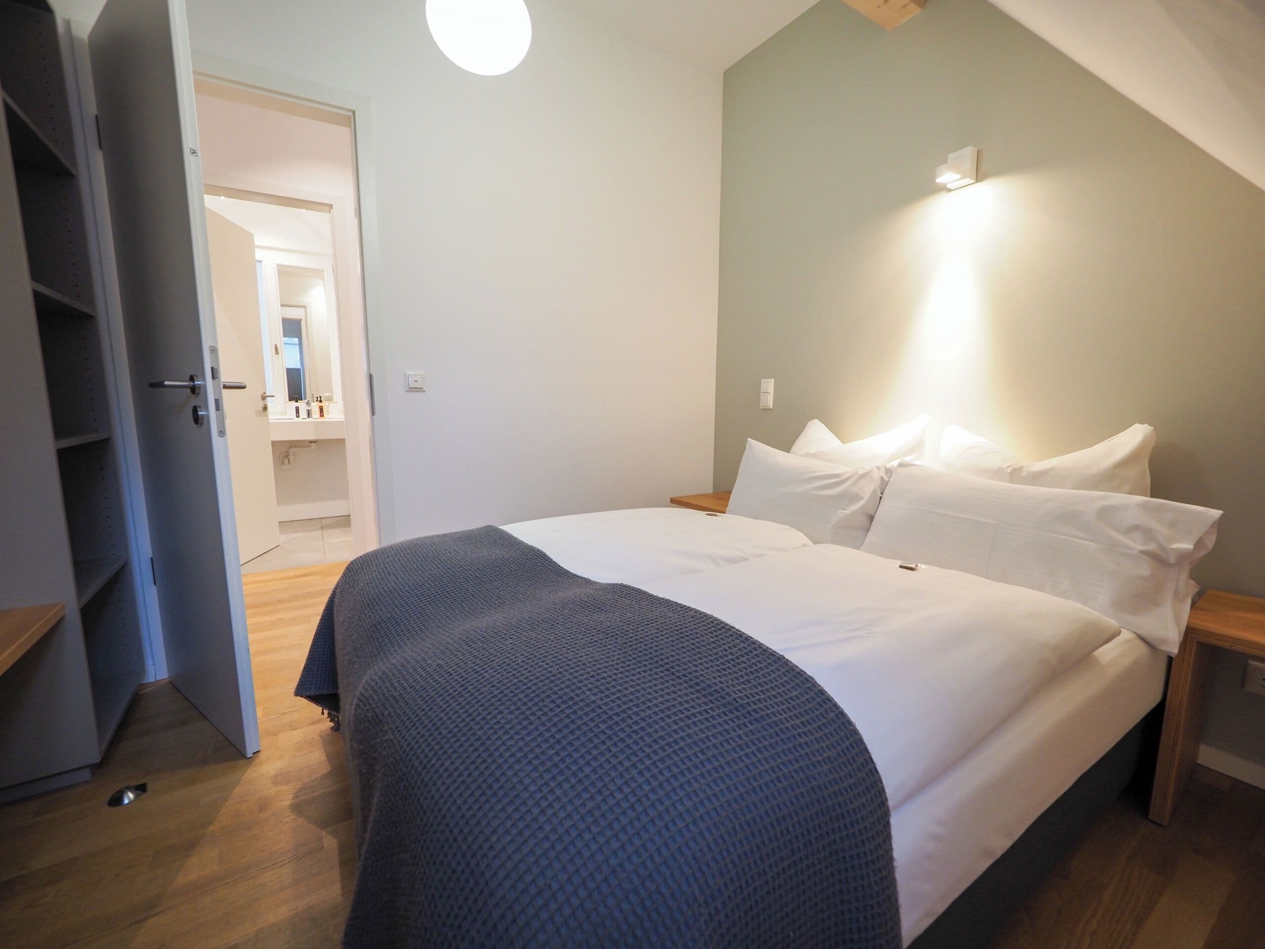 Ein Schlafzimmer mit einem Bett, einem Nachttisch und einem Beistelltisch. Eine Tür führt zu einem Badezimmer.