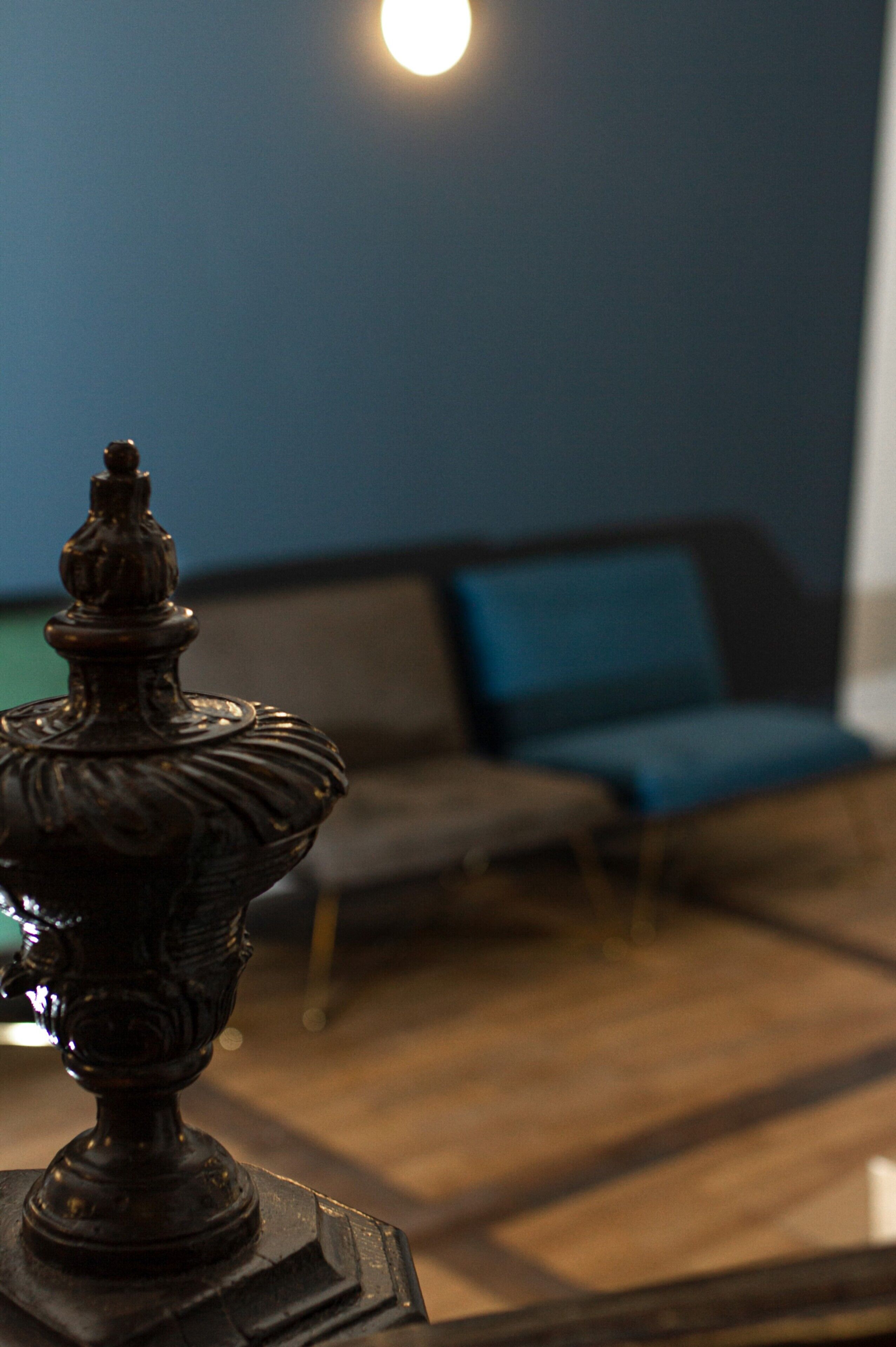 A close-up of a decorative object, possibly a lamp, with a blurred background featuring a blue sofa and a wooden floor.