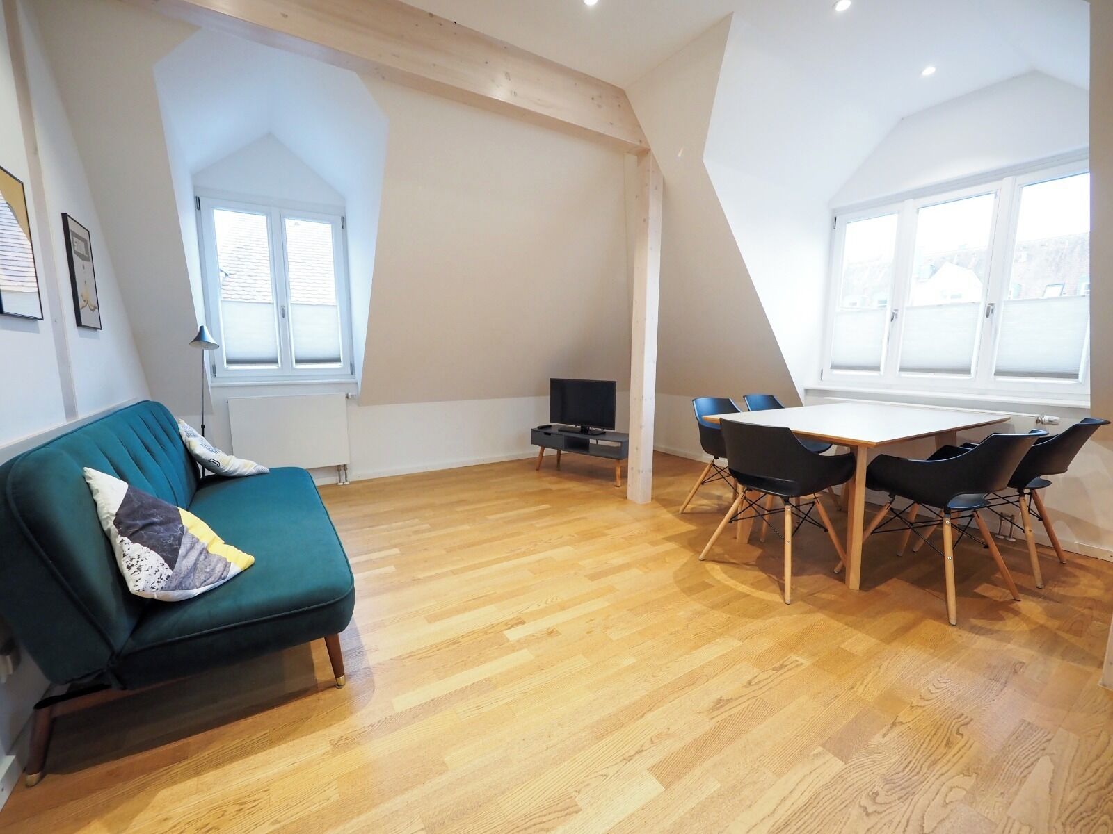 A modern living space with a sofa, a dining table with chairs, a TV, and a window.