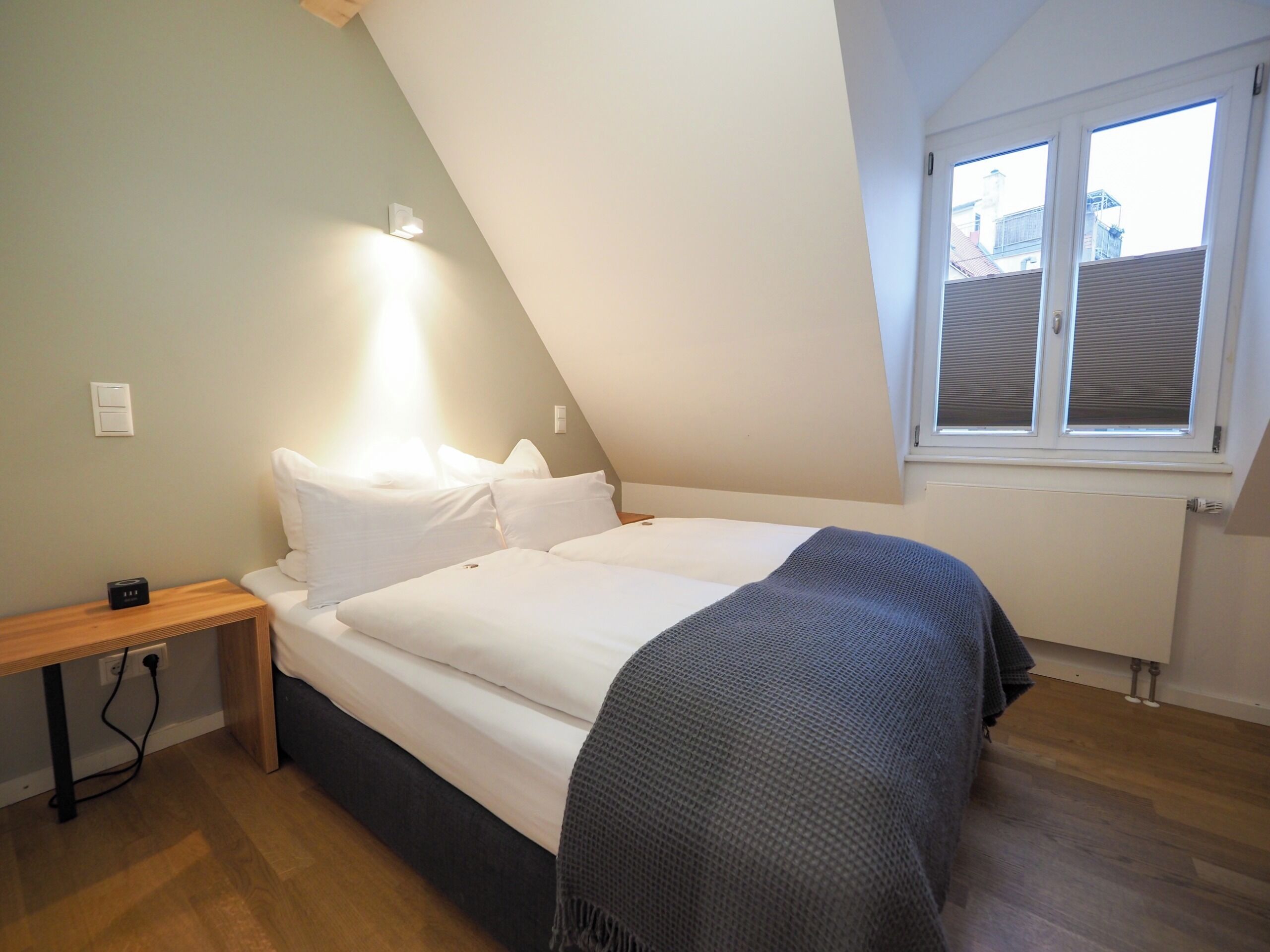 A bedroom with a bed, a bedside table, a lamp, a window, and a radiator.