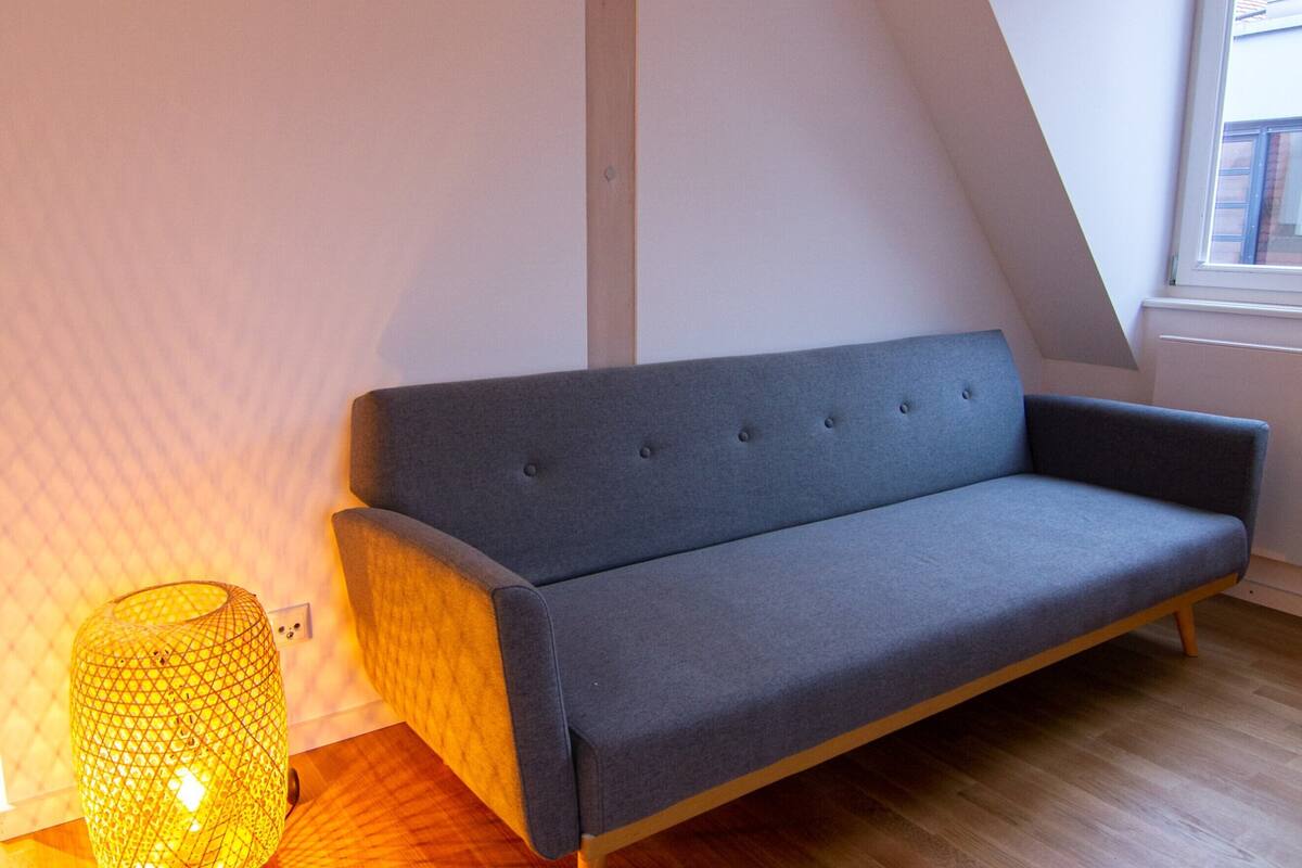 Una habitación moderna con un sofá gris, suelo de madera y una lámpara amarilla.