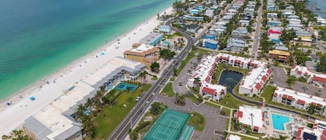 An aerial view of a coastal resort with a beachfront, a tennis court, and a pool area.