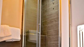 A modern bathroom with a glass-enclosed shower, a towel rack, and a radiator.