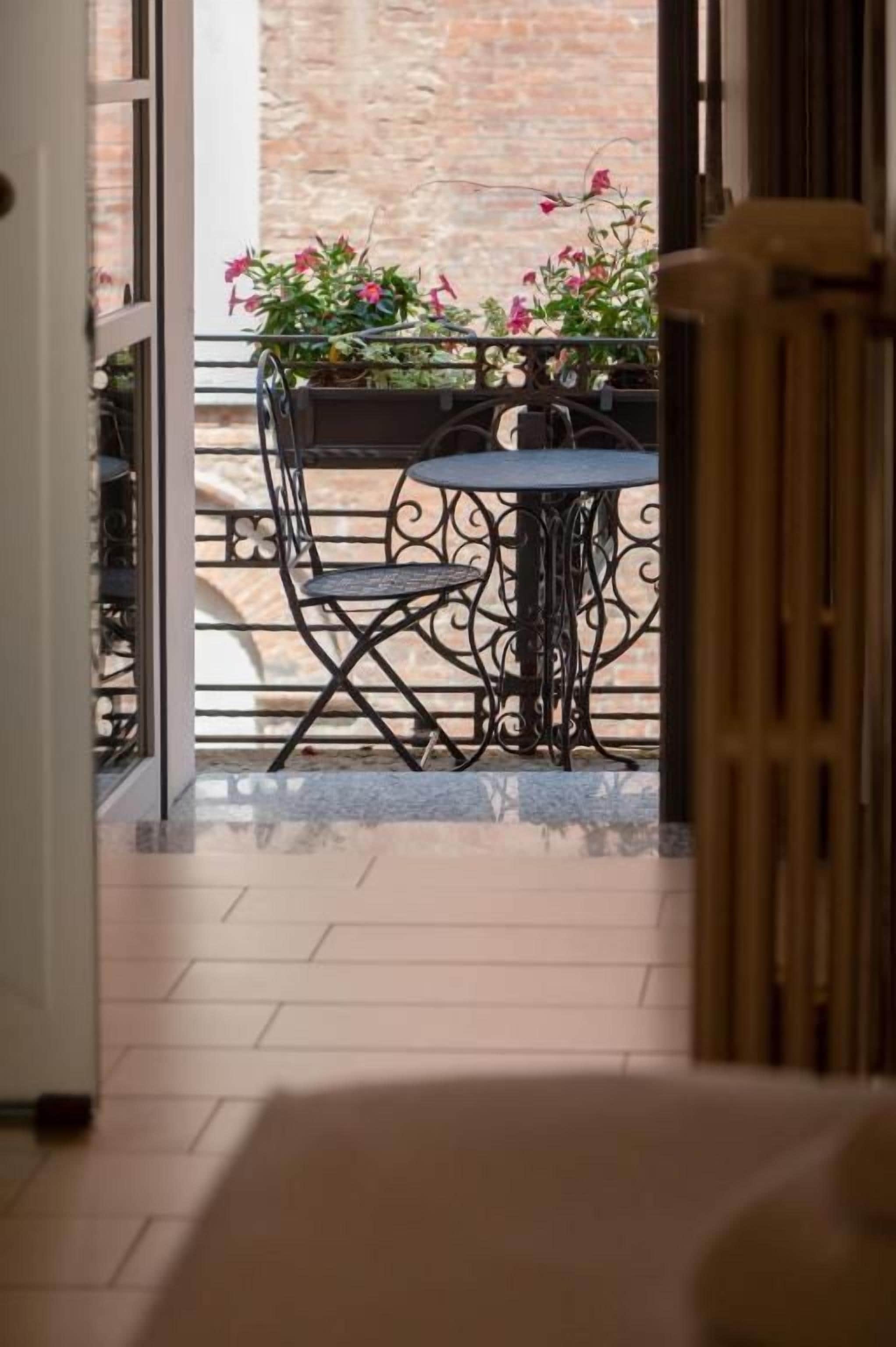 A view of a balcony with a table and chairs, a potted plant, and a brick wall in the background.