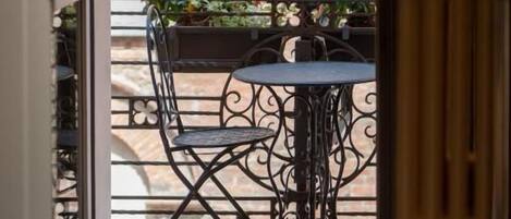 A view of a balcony with a table and chairs, a potted plant, and a brick wall in the background.