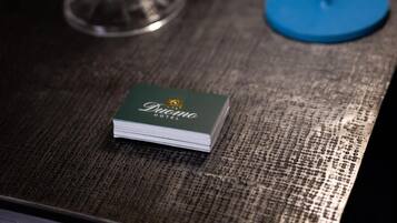 Un piccolo libretto verde con la scritta "Diana Hotel" su una superficie strutturata, con una lampada blu e un vaso di vetro decorativo con una pianta sullo sfondo.