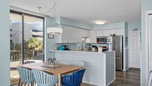 A modern kitchen with white cabinets, a wooden dining table, and blue chairs. - Oceanfront w/ Elevator, Indoor Pool/Hot tub (North Myrtle Beach)