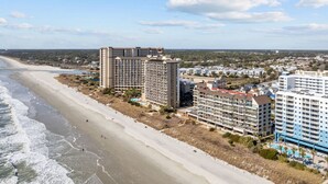 A beachfront hotel with multiple high-rise buildings, a sandy beach, and a clear view of the ocean. - Oceanfront w/ Elevator, Indoor Pool/Hot tub (North Myrtle Beach)