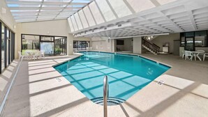 An indoor swimming pool with a glass ceiling, surrounded by white chairs and tables. - Oceanfront w/ Elevator, Indoor Pool/Hot tub (North Myrtle Beach)