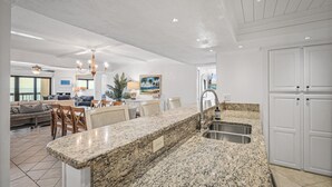 A spacious kitchen with granite countertops, a built-in sink, and white cabinetry. - Luxury direct oceanfront 3/3 corner penthouse with heated pool and garage parking (Ormond Beach)