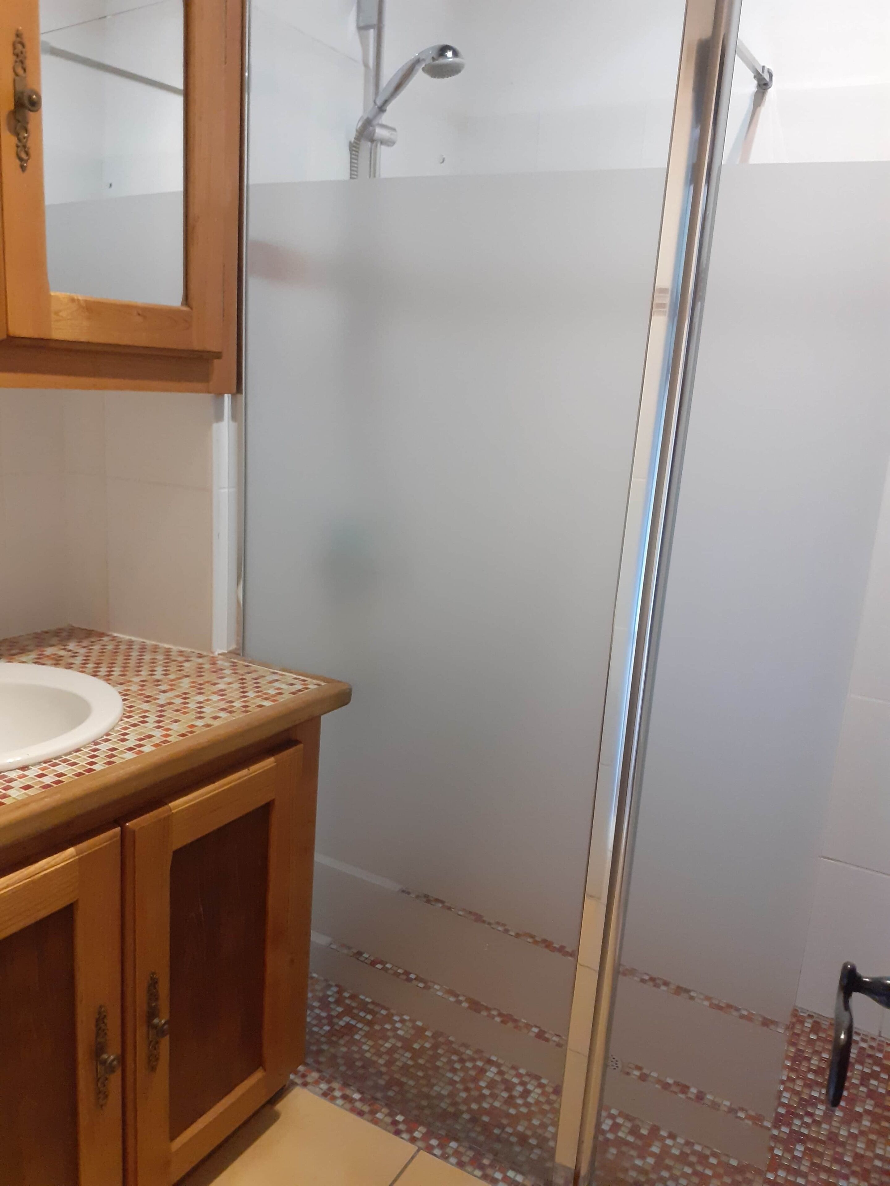 A bathroom with a wooden vanity, a glass shower enclosure, and a tiled floor.