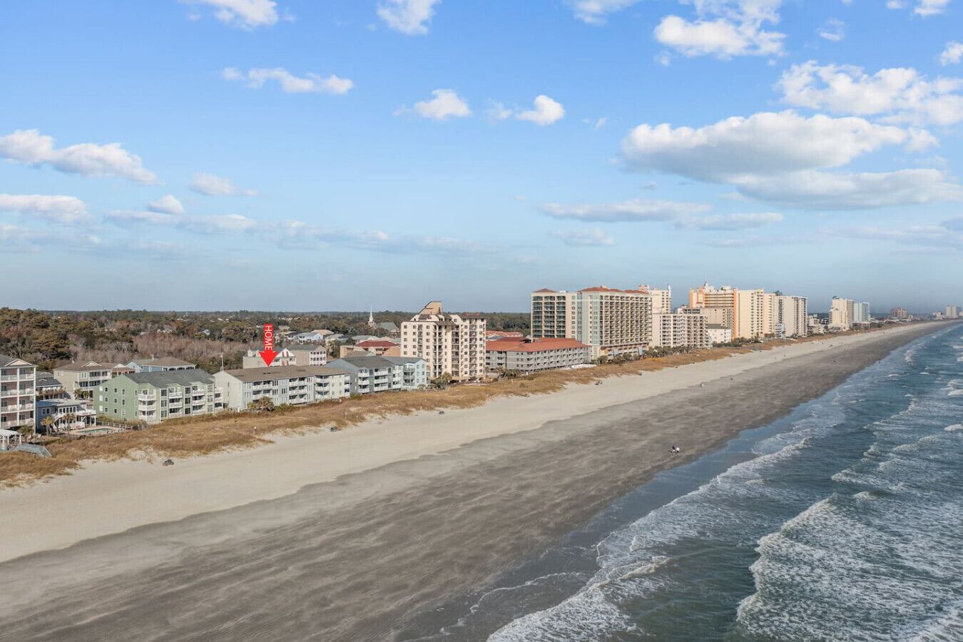 Et kysthotel med flere bygninger langs stranden, en sandstrand og bølger.