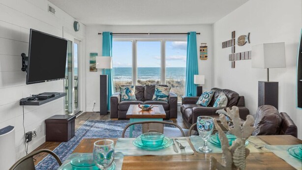 A living room with a view of the ocean, furnished with leather sofas and a wooden coffee table. - Immaculate 3/2 Oceanfront Condo near Main St, Pool (North Myrtle Beach)