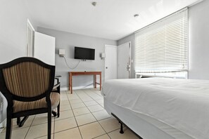 Une chambre d’hôtel avec un lit, un bureau, une chaise, un téléviseur fixé au mur et une fenêtre avec des stores.