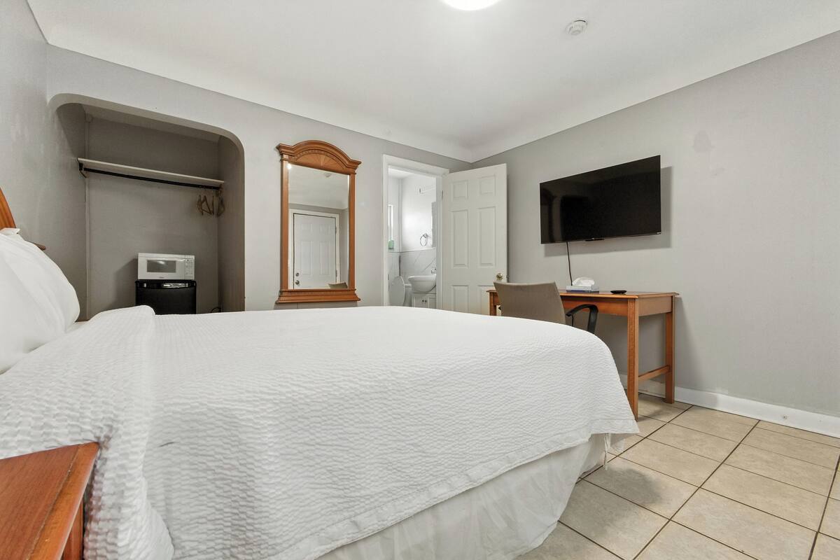 Quarto com uma cama grande, televisão na parede, escrivaninha e espelho.