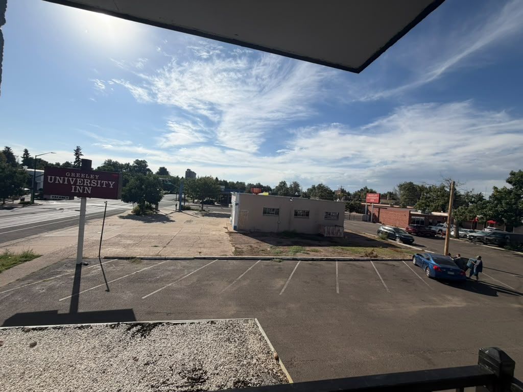 Um estacionamento com uma placa indicando 'Greeley University Inn' e um pequeno edifício ao fundo.