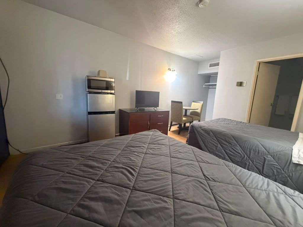 A hotel room with two beds, a television, a desk, and a microwave.