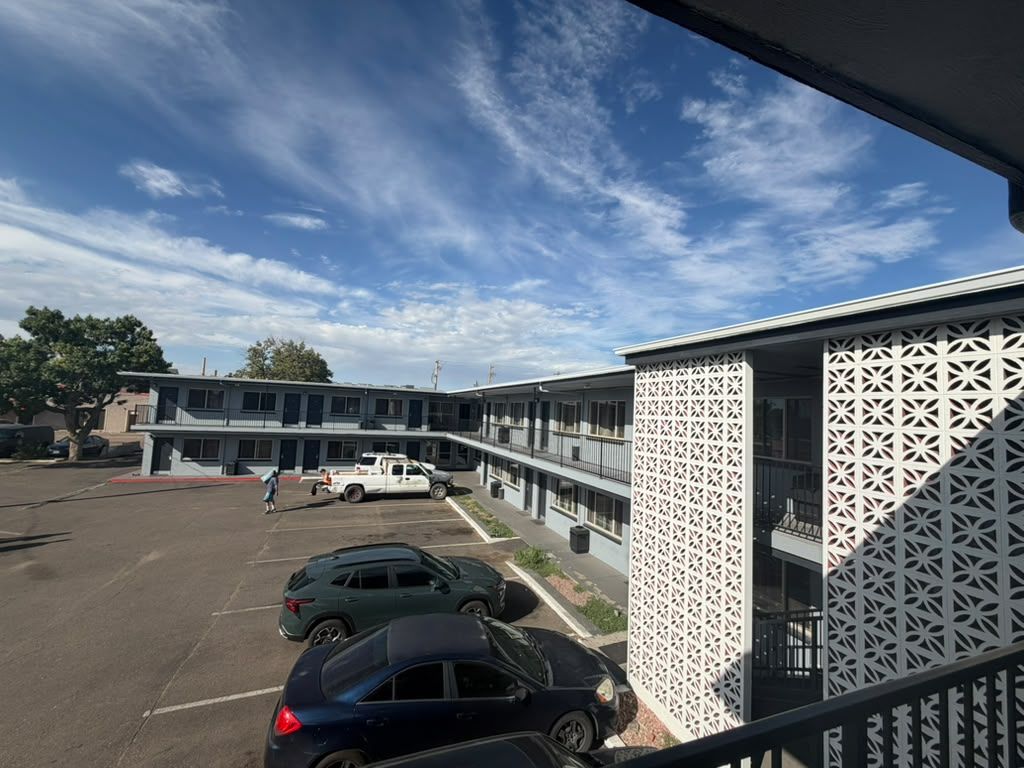 A parking lot with several cars, a building with a patterned facade, and a clear sky.