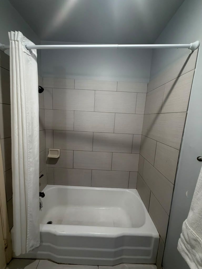 A small, enclosed shower area with a white bathtub, tiled walls, and a shower curtain.