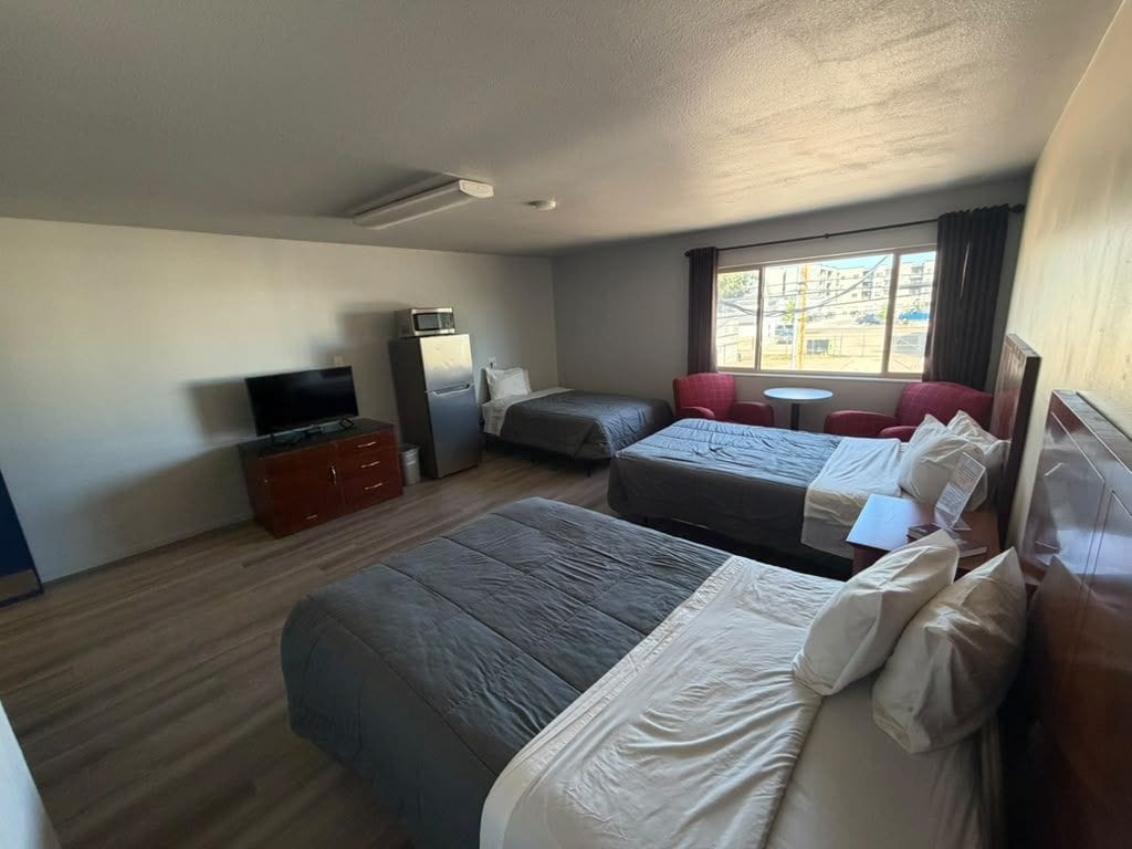 A hotel room with two beds, a TV, a desk, and a window with curtains.