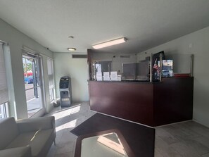 A reception area with a dark reception desk, a seating area with a chair, and a window with blinds.