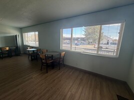 A room with a dining table and chairs, large windows with blinds, and a view of a street.