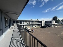 Um motel com galeria coberta, estacionamento e um edifício com várias janelas.