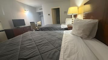 Quarto de hotel com uma cama, uma escrivaninha, uma cadeira, uma televisão e um abajur.