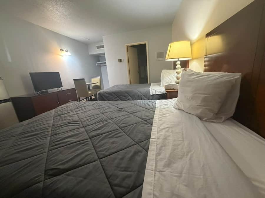 A hotel room with a bed, a desk, a chair, a television, and a lamp.