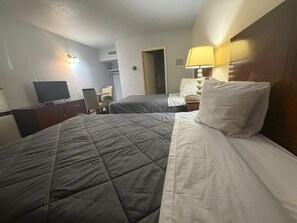 A hotel room with a bed, a desk, a chair, a television, and a lamp.