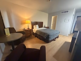 Una habitación de hotel con una cama, una mesita de noche, una lámpara, una silla y una pequeña mesa.