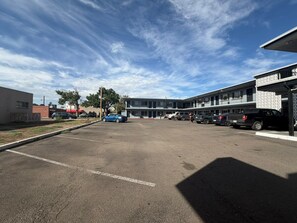 A parking lot with multiple cars, a building with a flat facade, and a clear sky. - Greeley University Inn By Capital O I-25 (Greeley)