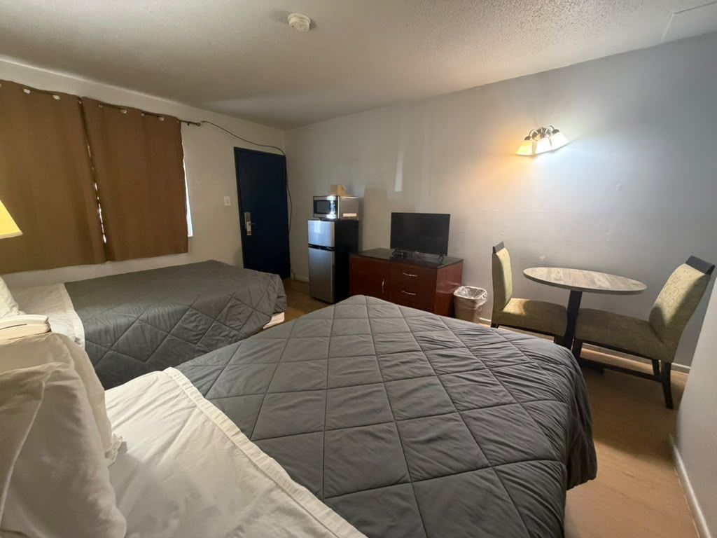 A hotel room with two beds, a desk with a television, a chair, and a small table.