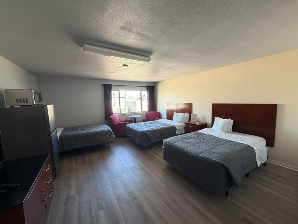 A hotel room with two beds, a desk, a chair, a TV, and a window.