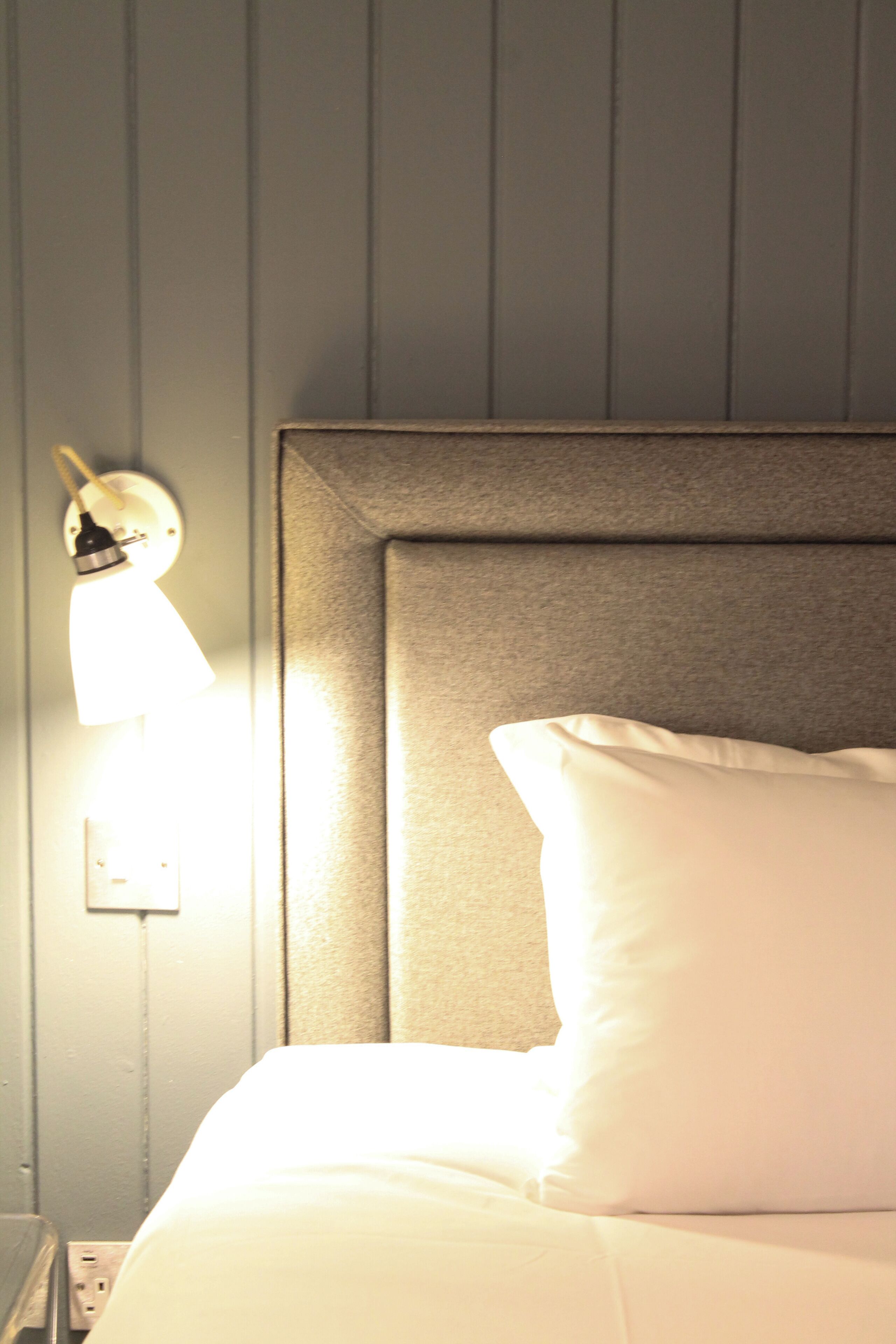 A neatly made bed with a headboard against a wall with vertical paneling.