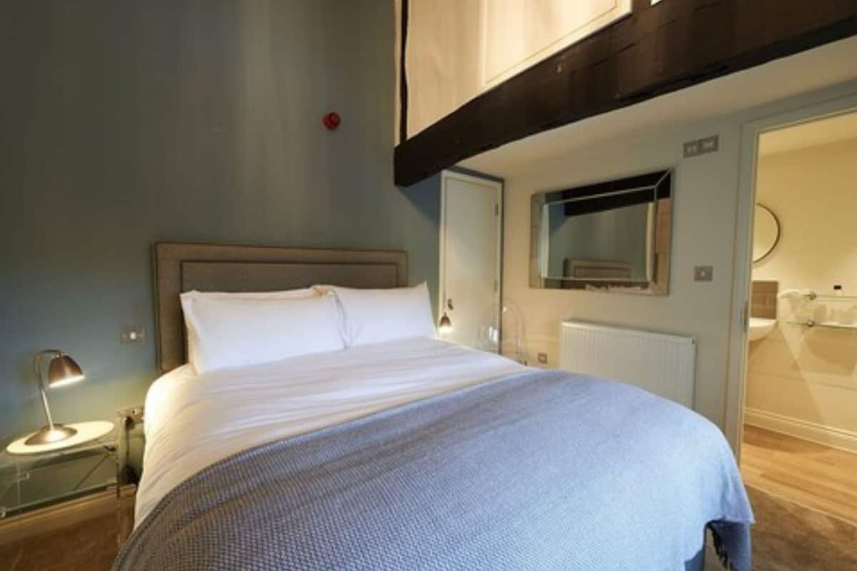A hotel room with a bed, bedside table, lamp, and a mirror on the wall.