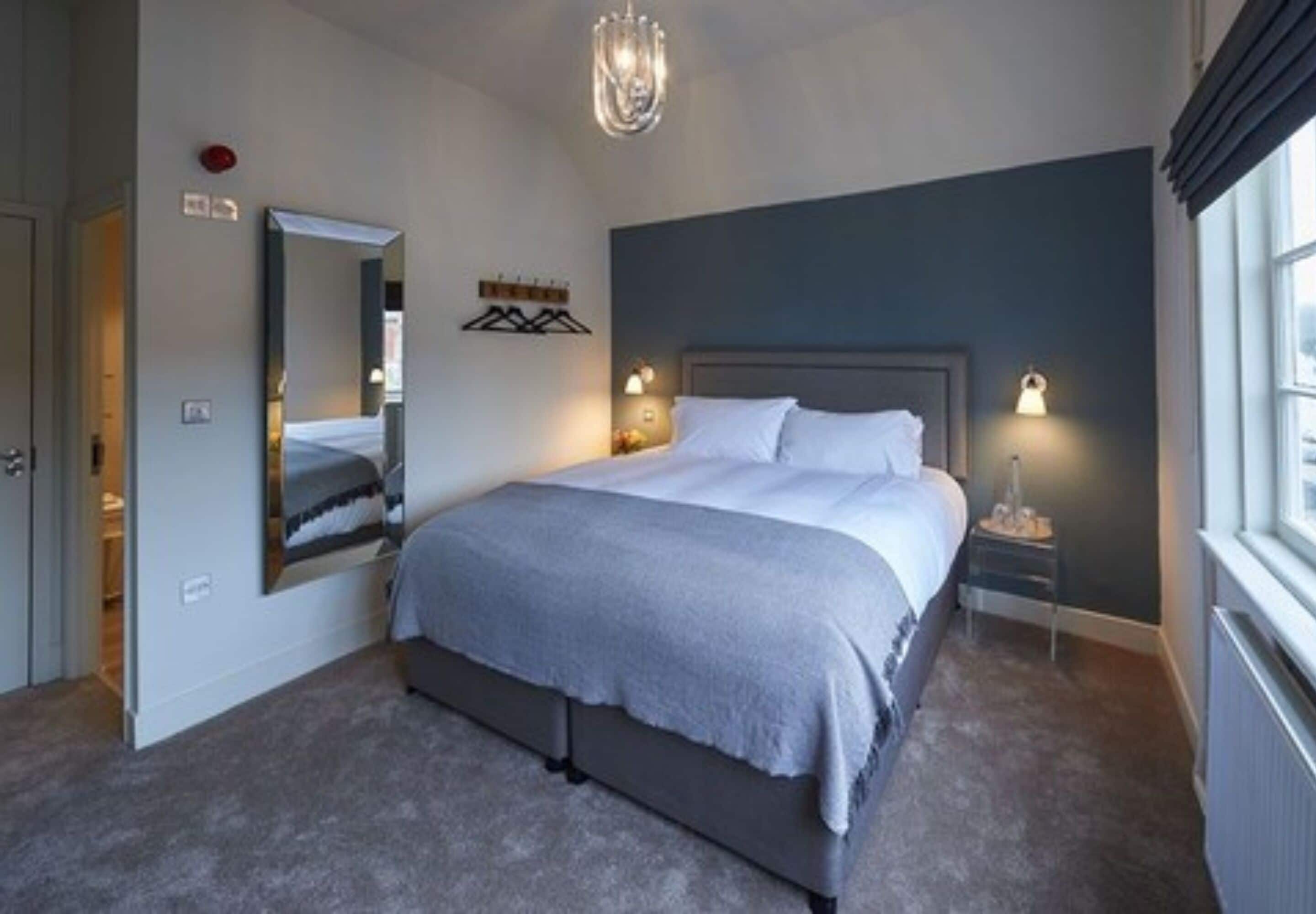 Ein Schlafzimmer mit einem großen Bett, Nachttischlampen, einem Spiegel und einem Fenster.