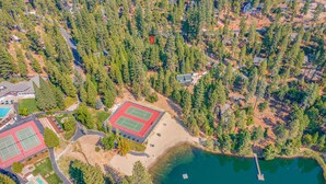 Eine Vogelperspektive zeigt eine Wohngegend mit Tennisplatz, Schwimmbad und einer anlegenden Mole im See.