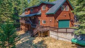 Eine zweistöckige Blockhütte mit einer grünen Garage, einer überdachten Terrasse und einer Treppe, die zum Obergeschoss führt.