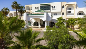Een modern hotel met een centraal binnenhof, palmbomen en een mediterrane architectuur.