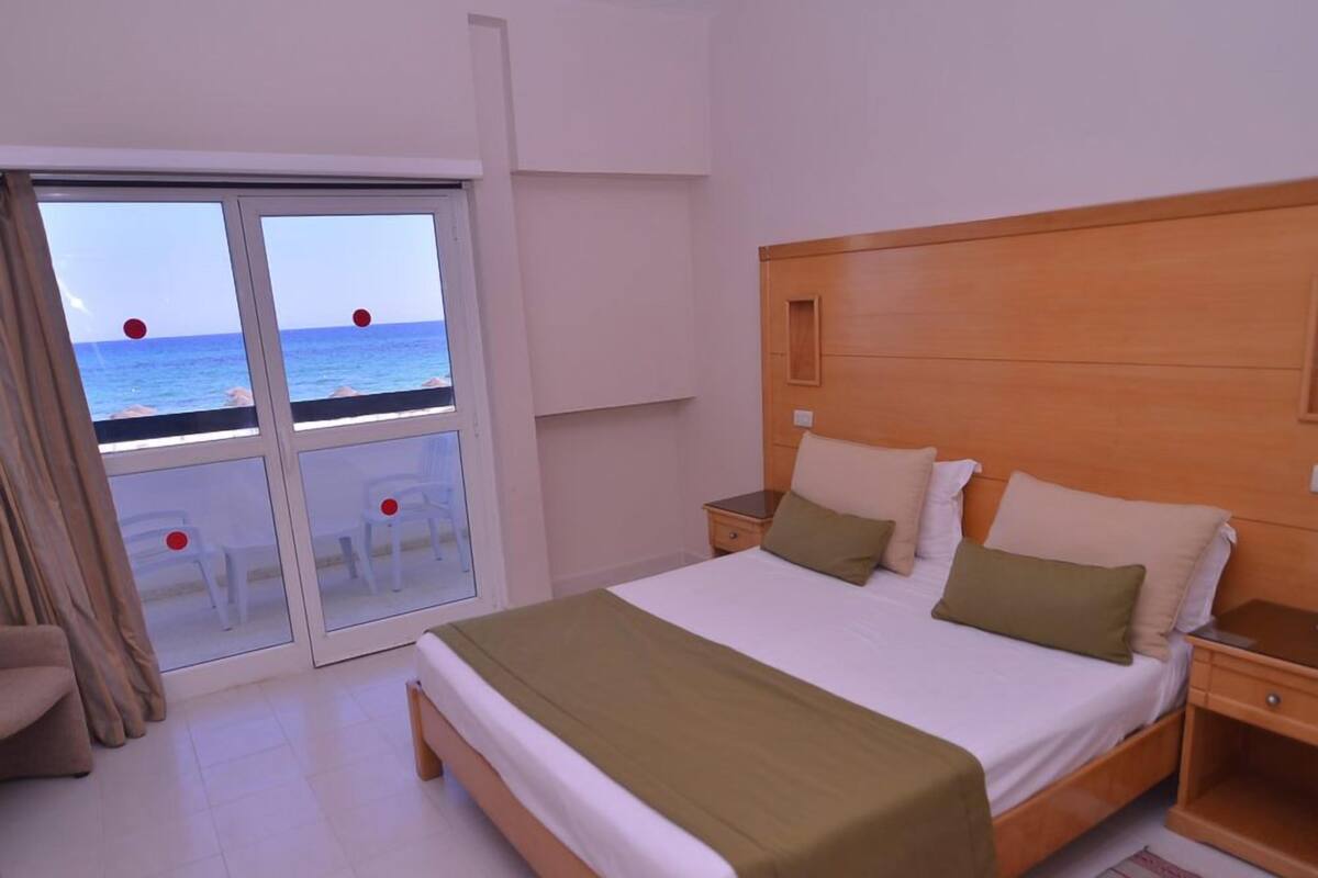 Een slaapkamer met een groot bed, een houten hoofdbord en uitzicht op zee door een schuifdeur.