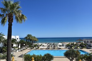A resort pool area with a clear view of the sea, surrounded by palm trees and lounge chairs.