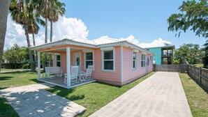 A single-story house with a porch and a small deck, surrounded by a well-maintained lawn and a wooden fence. - Flirty Flamingo, Too! 1 BDR 1BTH, with Shared in-ground pool! (Gulfport)